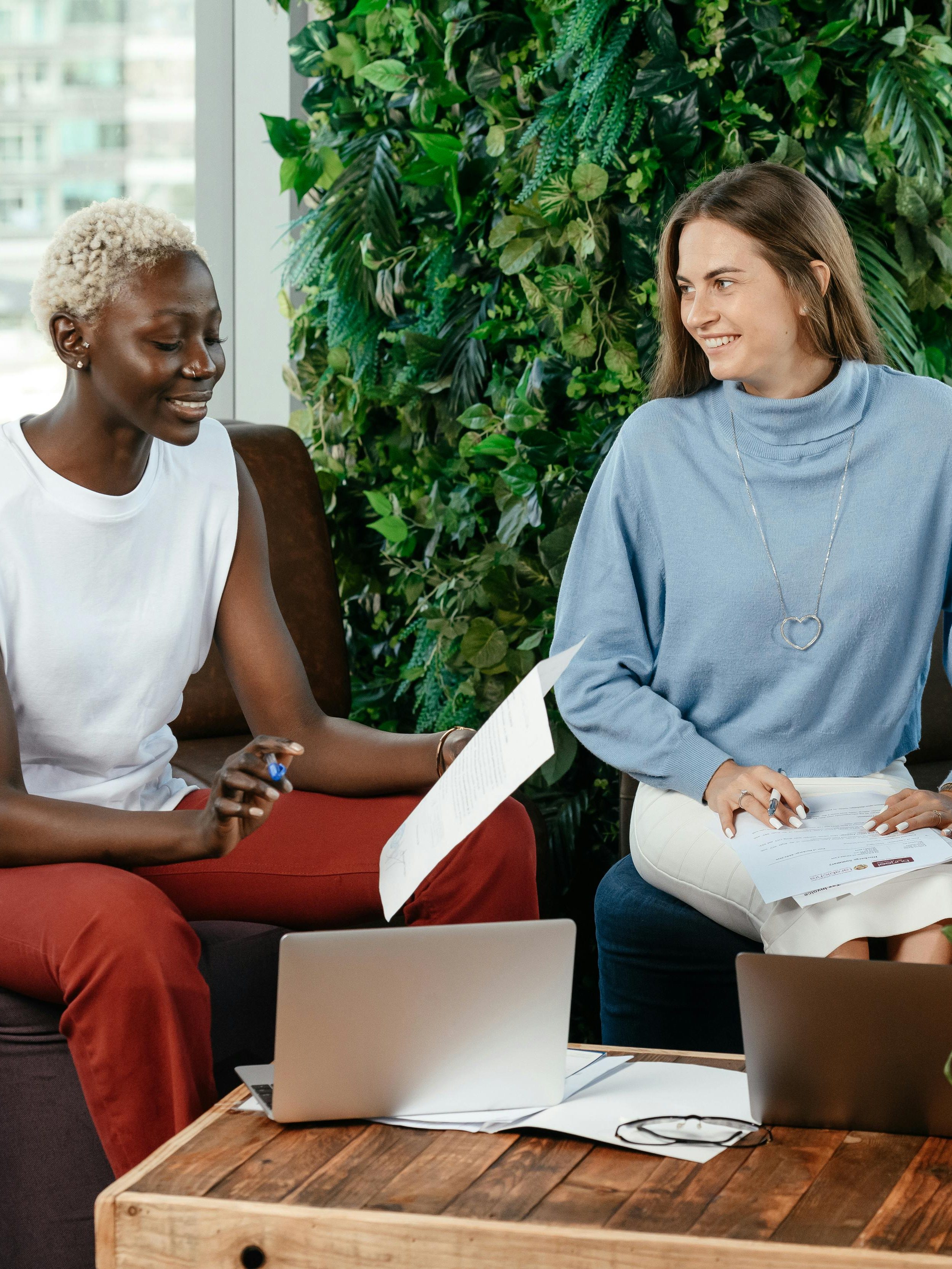 Deux jeunes femmes souriantes et détendues discutant autour de documents et d'un ordinateur